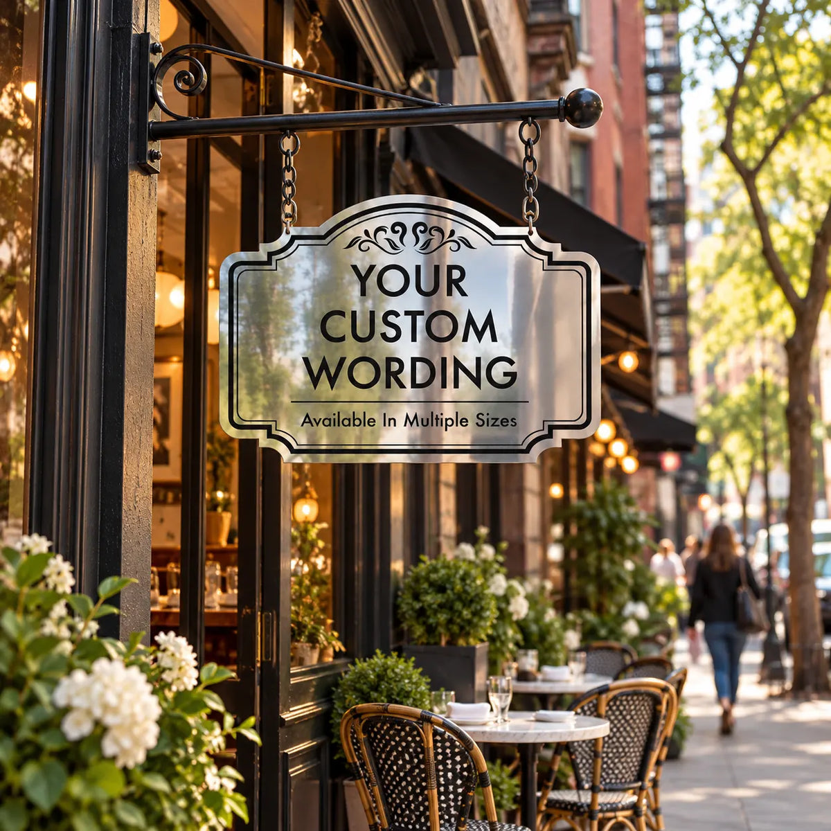 Custom double-sided mirror finish aluminum hanging sign in the Ornate Scroll design on a black iron bracket outside a sidewalk café