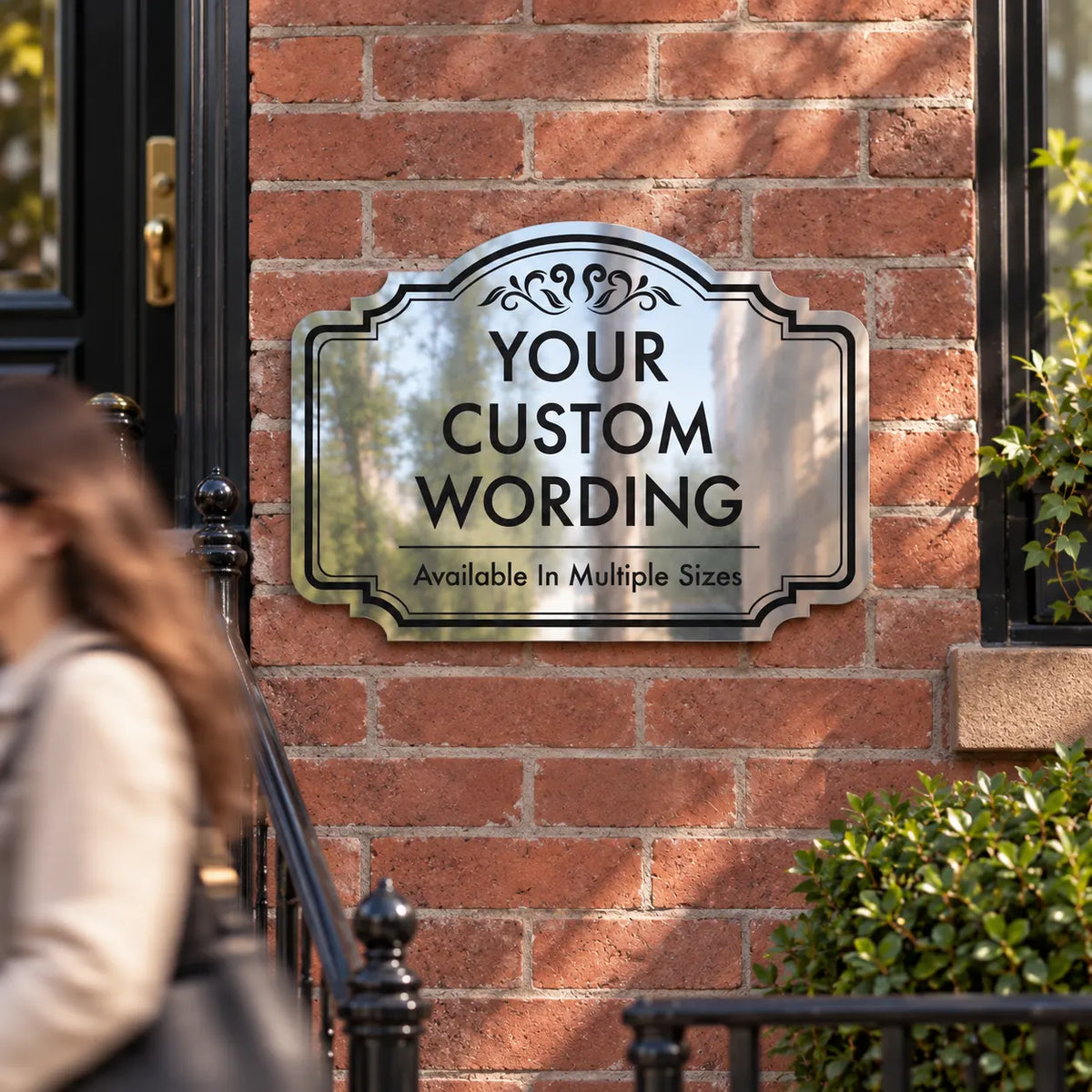 Mirror finish aluminum storefront sign with ornate border on a brick wall next to a doorway