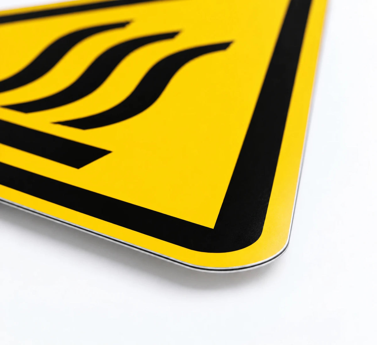 A close-up of a yellow warning sign with black border and three wavy lines, photographed on a clean white background.