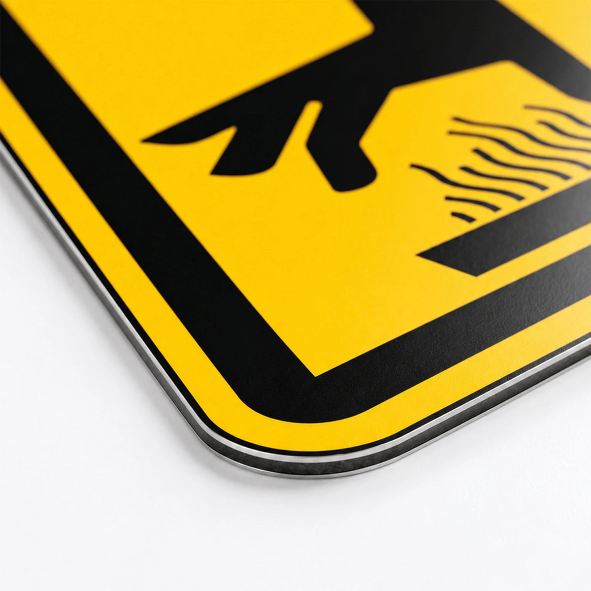 Close-up of a yellow and black warning sign with rounded corners, showing part of a black symbol on a bright yellow background.