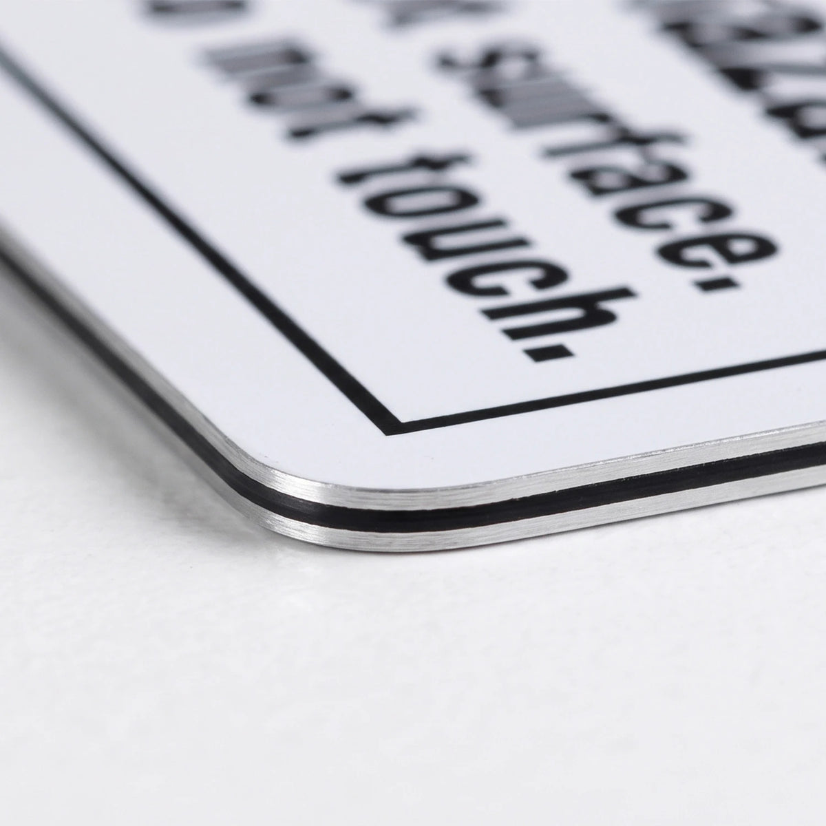 A close-up of a white metal sign with black text reading 'do not touch.' and a border, resting on a white surface.