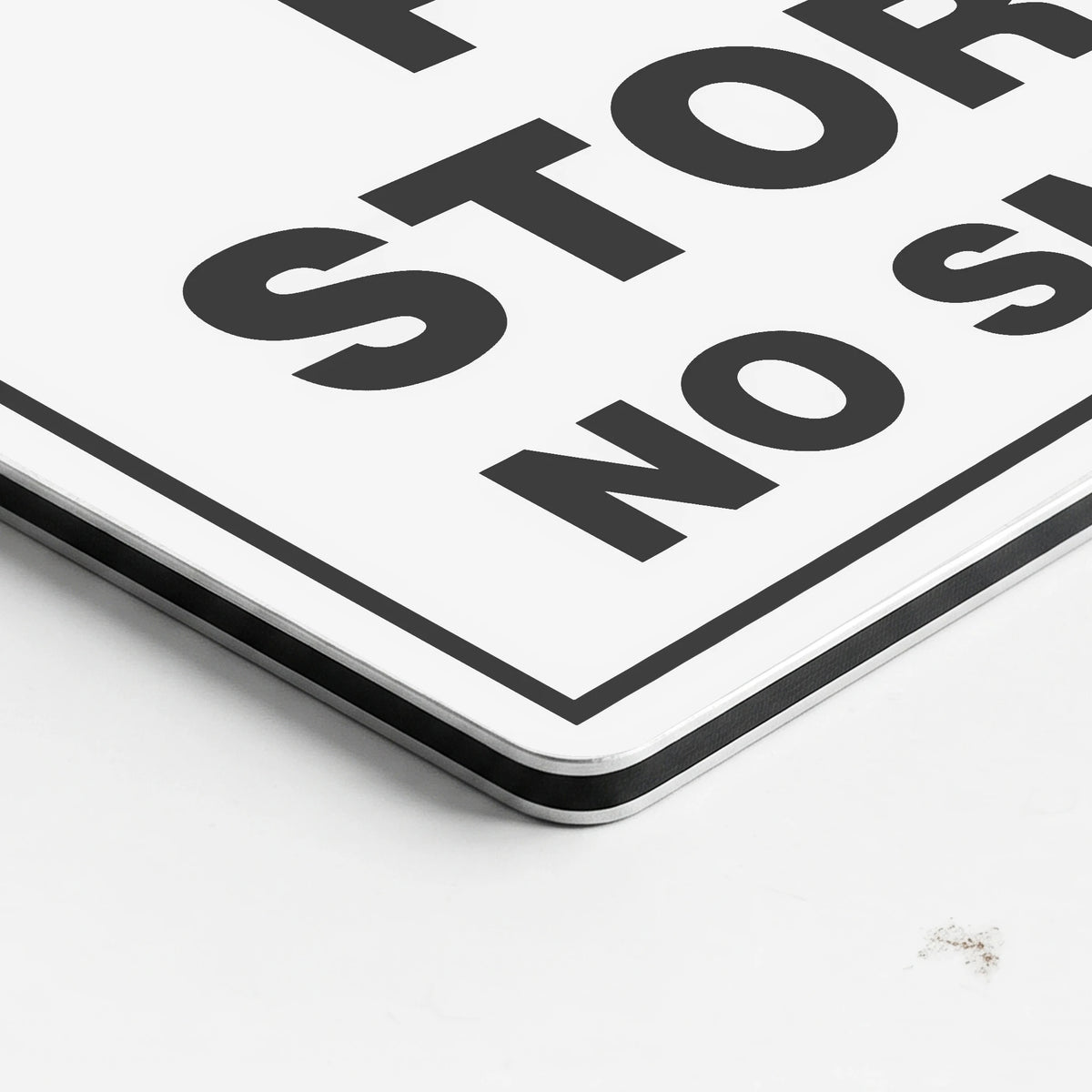 A close-up of a white rectangular sign with bold black text reading 'STOP' and 'NO' along a thin black border, photographed on a white surface.