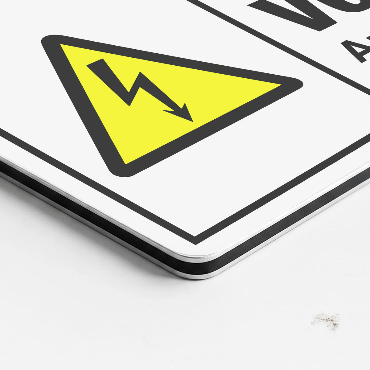 A close-up of a white warning sign featuring a yellow triangle with a black lightning bolt symbol, photographed on a white surface.