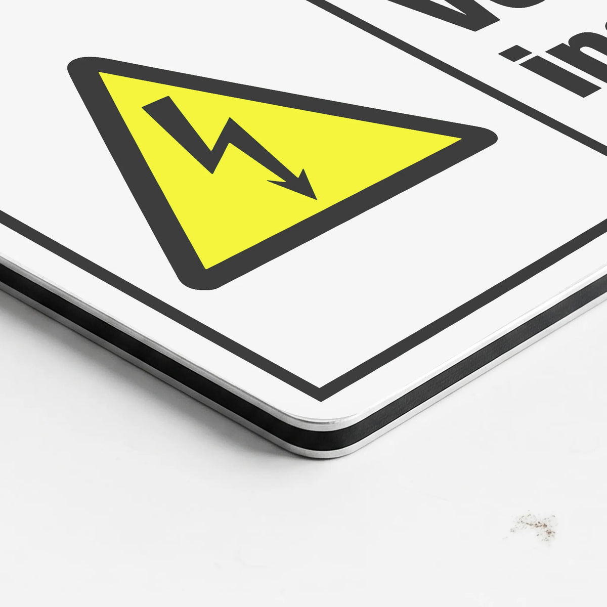 A close-up of a white warning sign with a yellow triangle and black lightning bolt symbol, photographed on a white surface.
