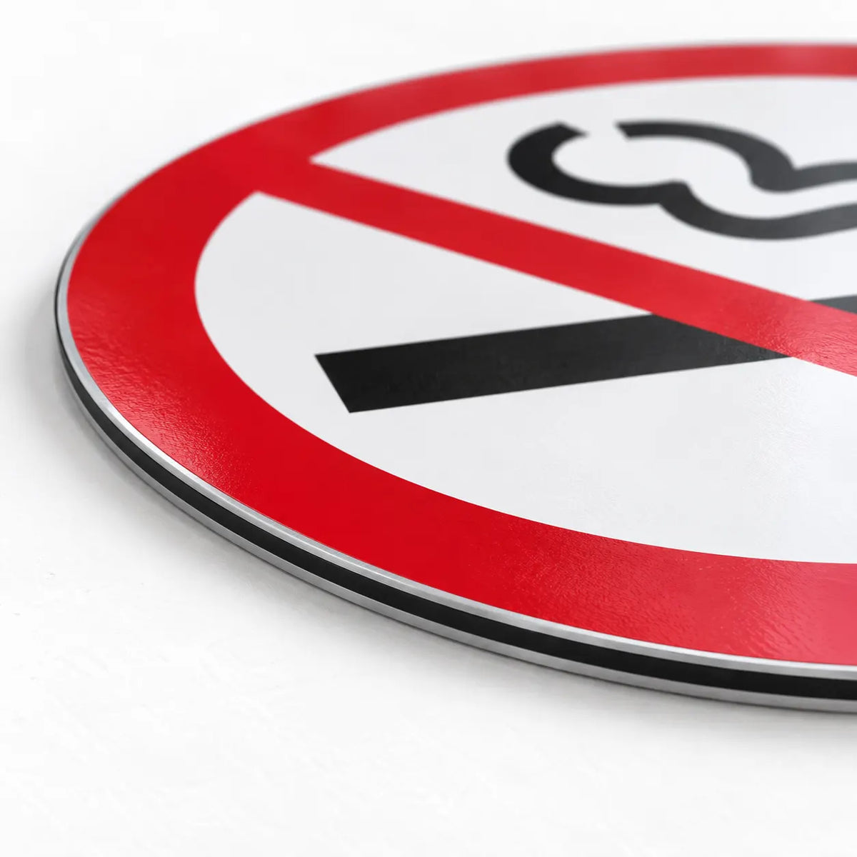 A close-up of a round prohibition sign with a red border, white center, black diagonal slash, and a black symbol on a light gray background.