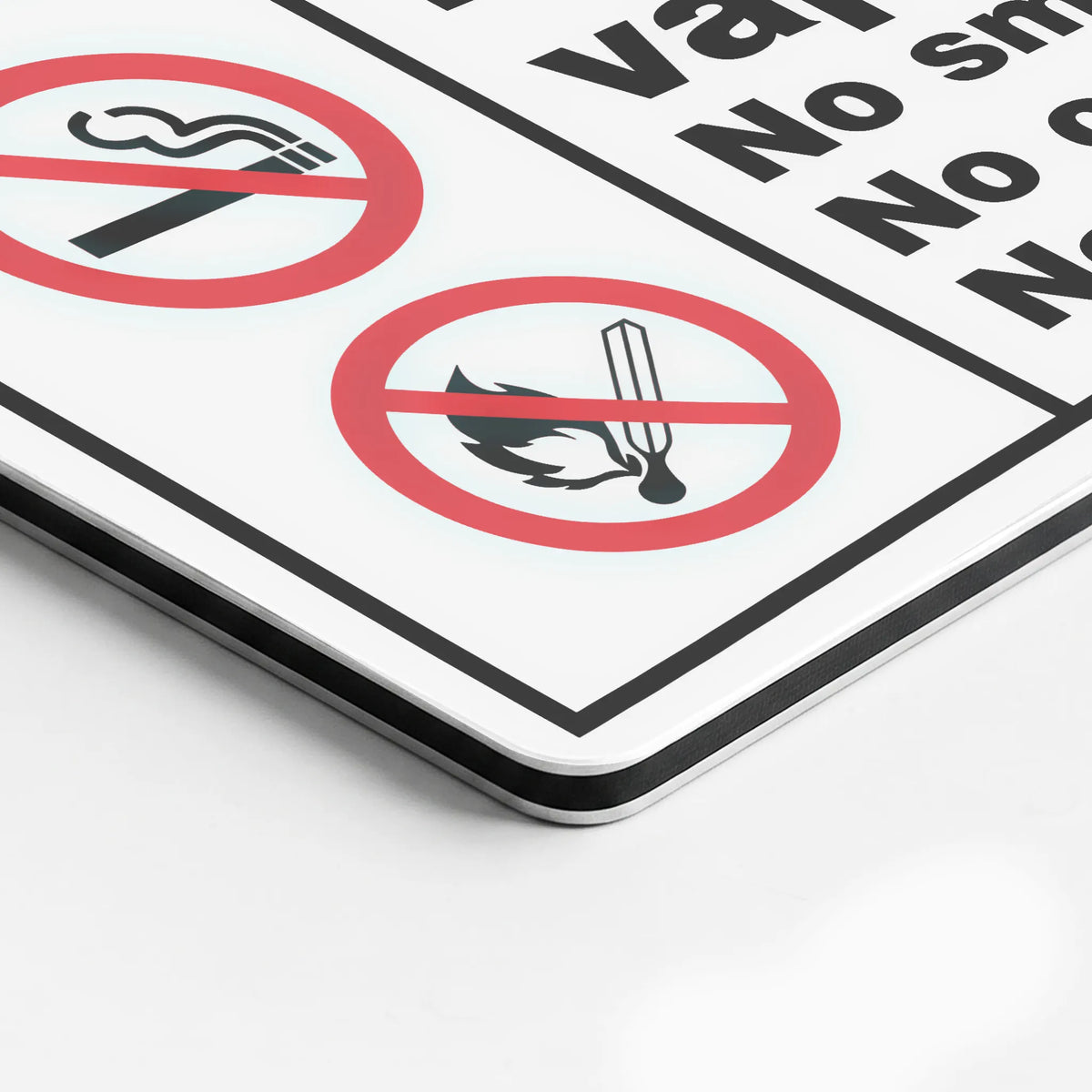 A close-up of a white safety sign with black text and red prohibition symbols, including a cigarette icon and a match icon crossed out, photographed on a light gray background.