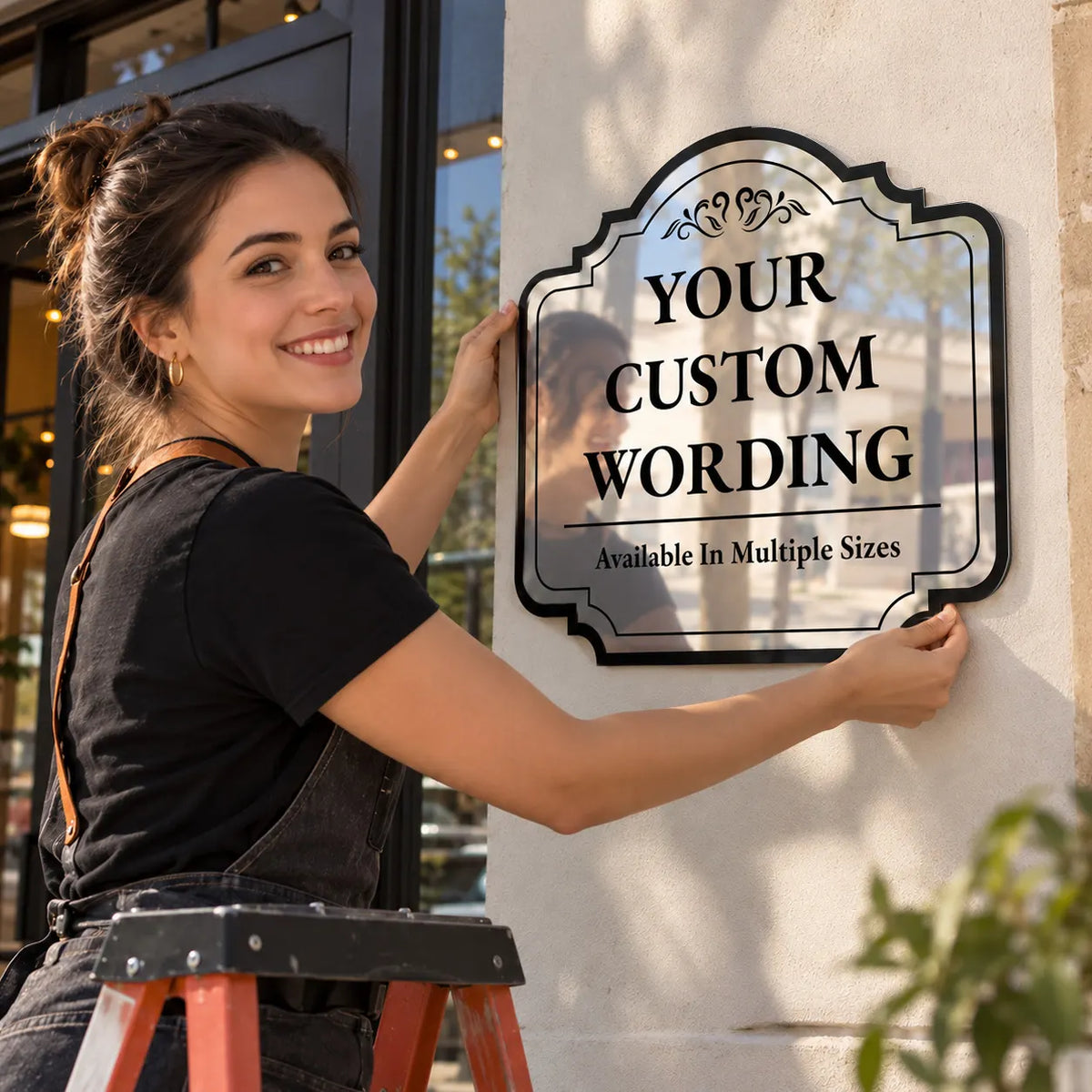 Woman on a ladder mounting a custom Ornate Scroll mirror finish aluminum sign on a storefront wall